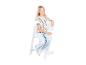 Blond meisje in gestreept shirt en jeans zit op een witte kinderstoel
