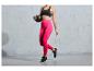 Een vrouw in roze leggings en een zwarte sportbeha houdt een fitnessbal vast.