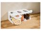Witte standaard met drie doorzichtige containers gevuld met bonen, linzen en koffiebonen op een houten aanrecht.