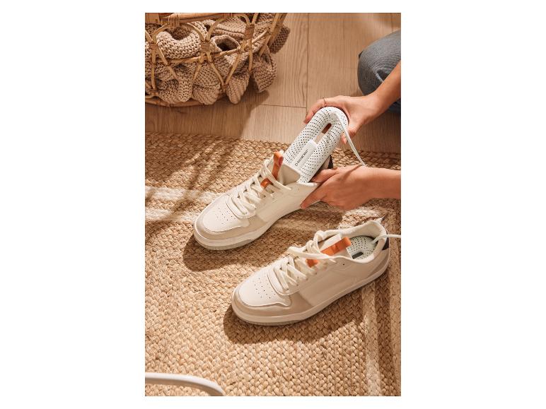 Une personne insérant un sèche-chaussures blanc dans une basket blanche sur un tapis tressé.