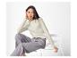 Femme en haut crème à manches longues et pantalon gris assise sur une chaise blanche.