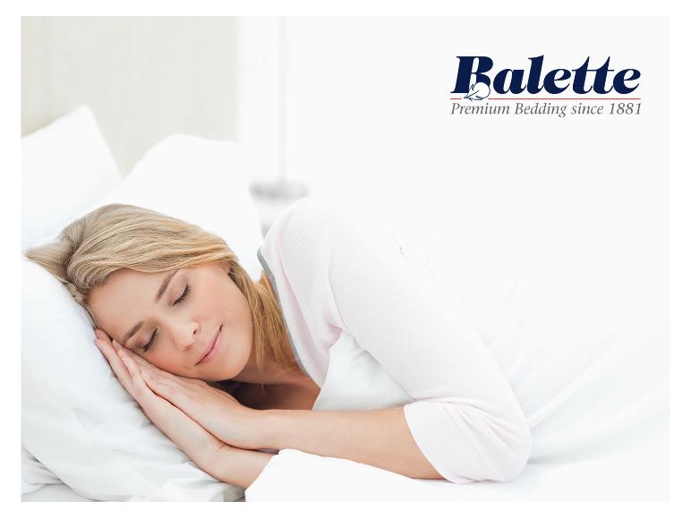 Vrouw slaapt op wit kussen en dekbed, met Balette Premium Bedding-logo.
