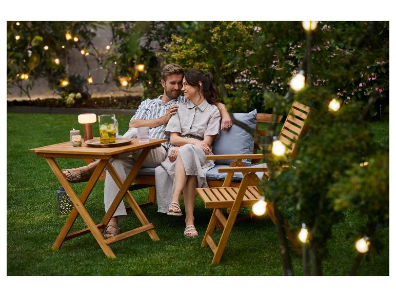 Koppel geniet van een avond in de tuin met buitenmeubilair en lichtslingers.
