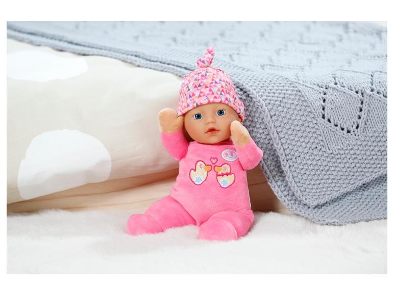 Baby born pop met roze outfit en muts op een wit pluche kleed.