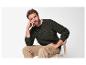 Homme en pull en maille vert foncé et pantalon kaki, assis sur une chaise.