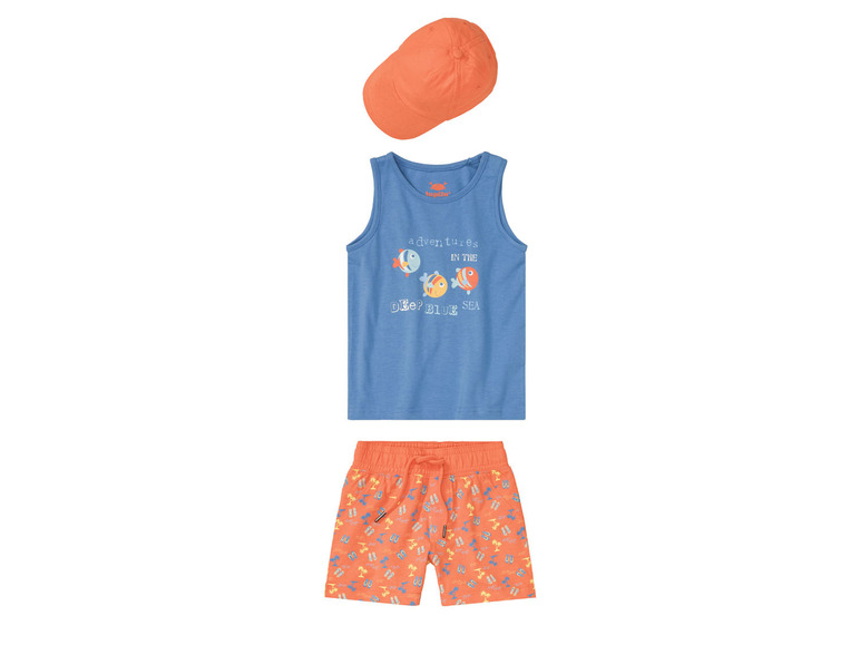 Un débardeur bleu avec un imprimé de poissons, un short de bain orange avec un imprimé de palmiers et une casquette orange.