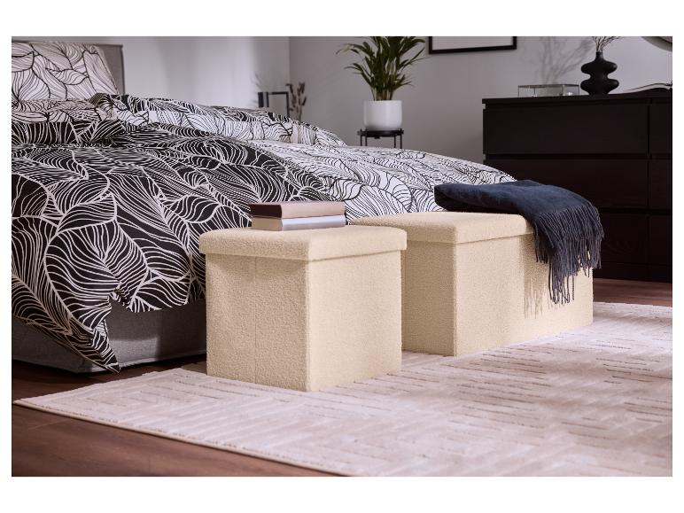 Slaapkamer met zwart-wit dekbedovertrek met bladpatroon, twee beige opbergpoefs en een vloerkleed.
