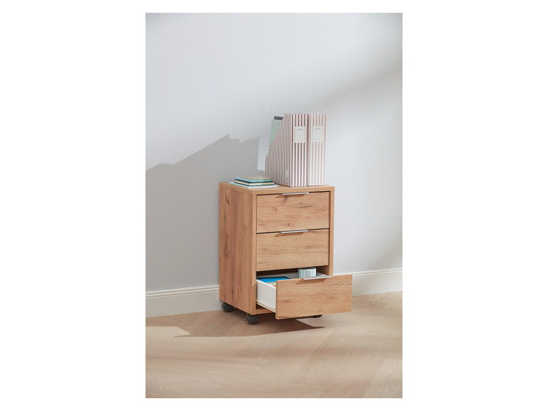 Un bureau en bois avec trois tiroirs sur roulettes, avec une pile de livres et deux dossiers sur le dessus.
