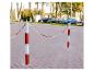 Rood-witte afzetpalen met ketting op een straat met geparkeerde auto's.