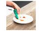 Main nettoyant une assiette avec une éponge à vaisselle sur une table en bois.