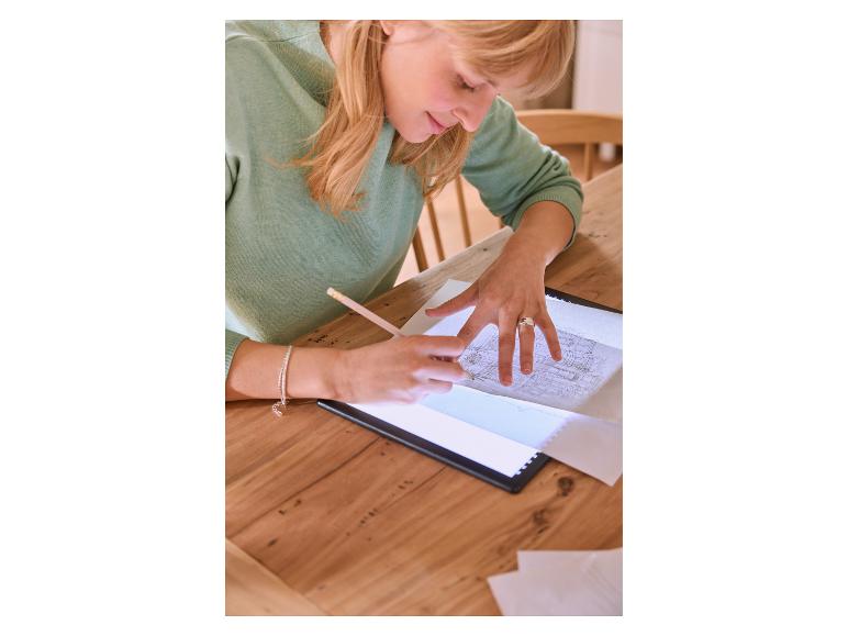 Femme traçant un dessin sur une tablette lumineuse avec un crayon sur une table en bois.