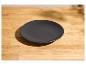 Assiette noire mate sur une table en bois clair avec des ombres.
