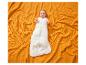 Baby in een witte slaapzak met gele patronen, liggend op een oranje wafel deken.