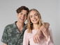 Een man en een vrouw in een groene en roze outfit, lachend naar de camera.