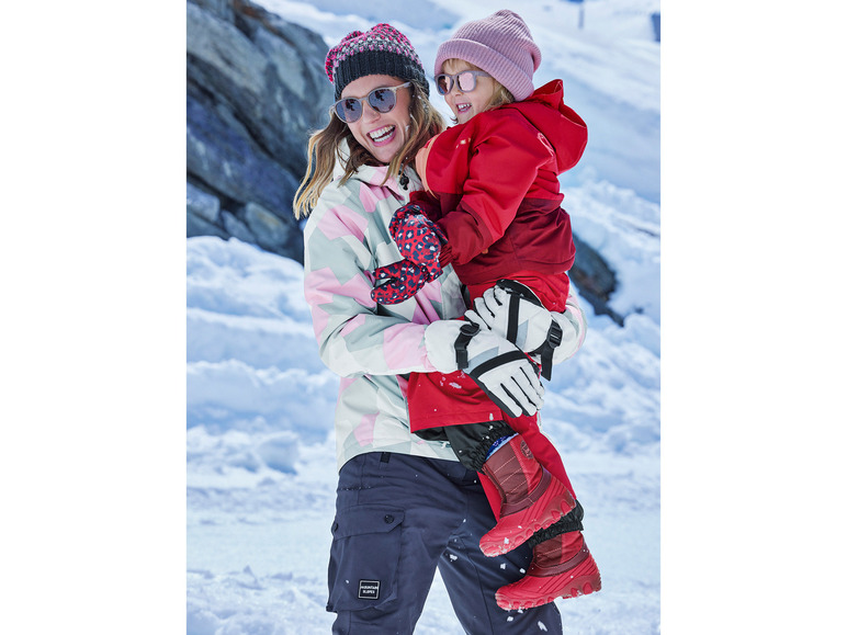 Een vrouw en een kind in winterkleding, inclusief een rode jas en 'Mountain Slopes' broek.