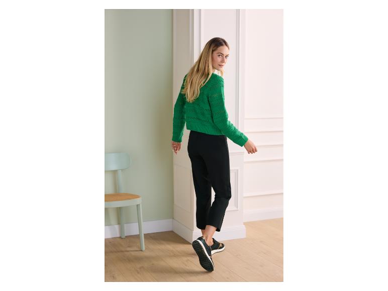Vrouw in groene gebreide trui en zwarte broek, loopt weg en kijkt achterom.