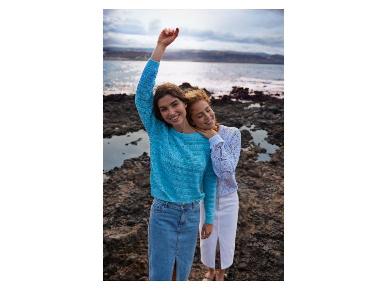Twee vrouwen in gebreide truien en denim rokken op een rotsachtig strand.