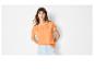 Femme en t-shirt orange brodé et short en jean clair.