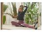 Femme en veste de sport noire et leggings violets s'étirant à l'intérieur avec des plantes.