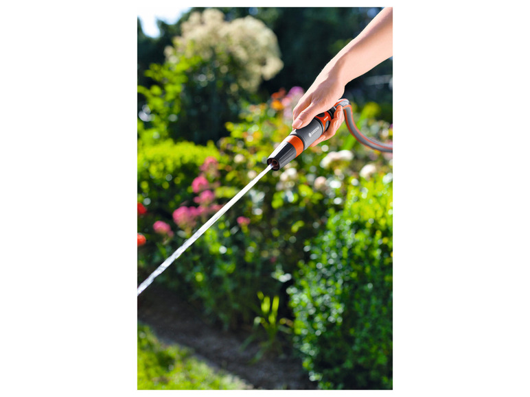 Een hand houdt een Gardena tuinslang vast en spuit water op een groene tuin.