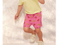 Een kind draagt een roze broek met tijgerprint en witte sneakers.