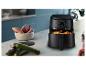 Zwarte airfryer met kippenpoten, zoete aardappelen en courgettes op een aanrecht.