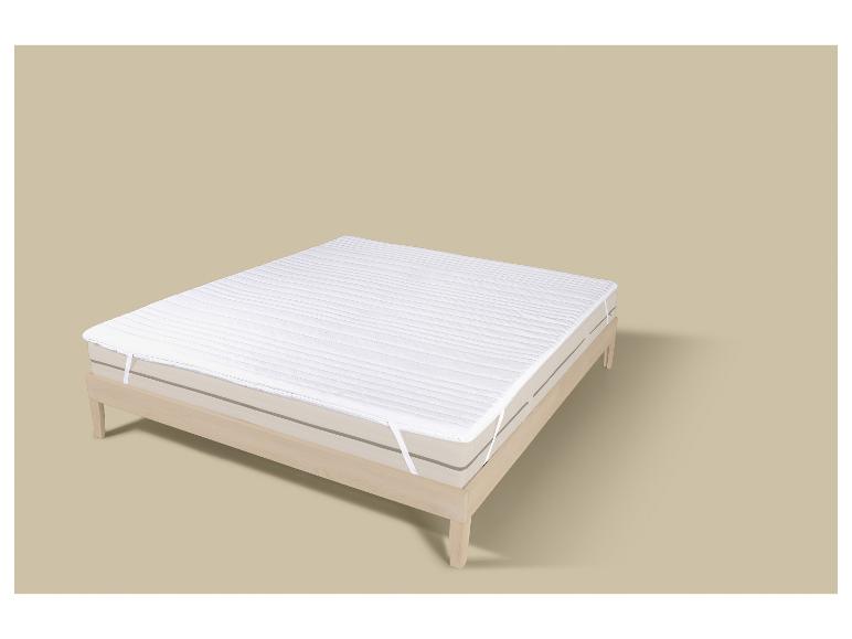 Witte matrasbeschermer op een licht houten bedframe