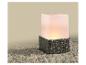 Vierkante lamp met gevlochten grijze basis en lichtgevende witte bovenkant op kiezels.