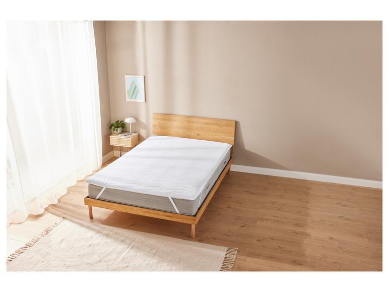 Un protège-matelas blanc sur un sommier en bois.