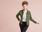 Een vrouw draagt een groene denimjas met een gestreept shirt en zwarte broek.