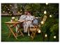 Couple assis sur un banc de jardin avec une table en bois, des boissons et des lumières.