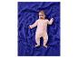 Un bébé souriant en grenouillère rose allongé sur une couverture bleue.