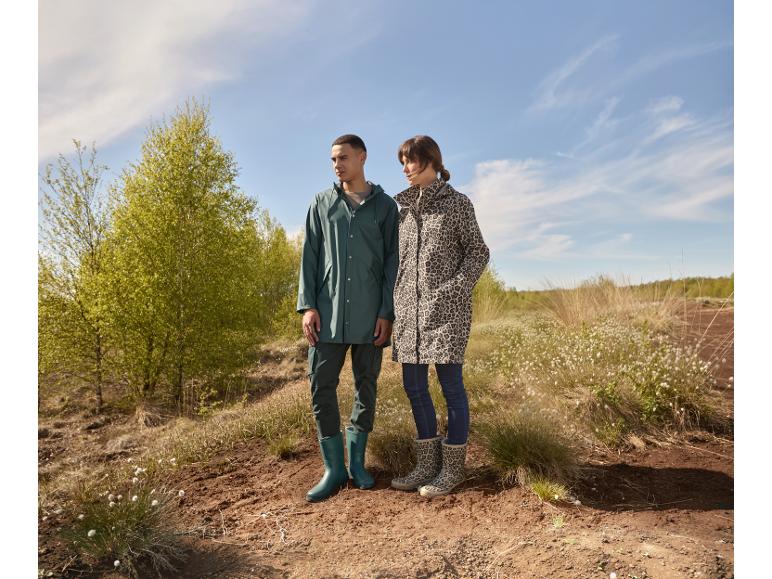 Man en vrouw in regenjassen en laarzen staan in de natuur.