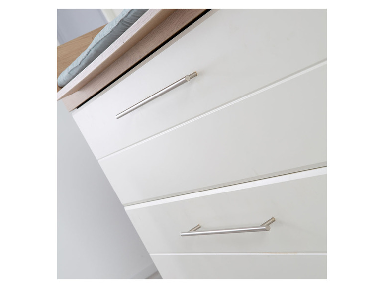 Commode blanche avec trois tiroirs et poignées argentées.