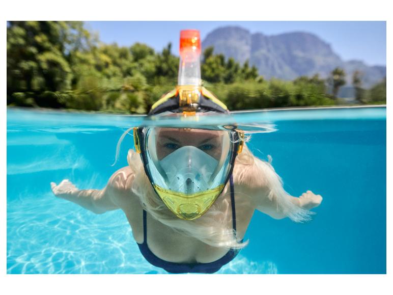 Vrouw met snorkelmasker en snorkel zwemt in een zwembad, met bergen en bomen op de achtergrond.