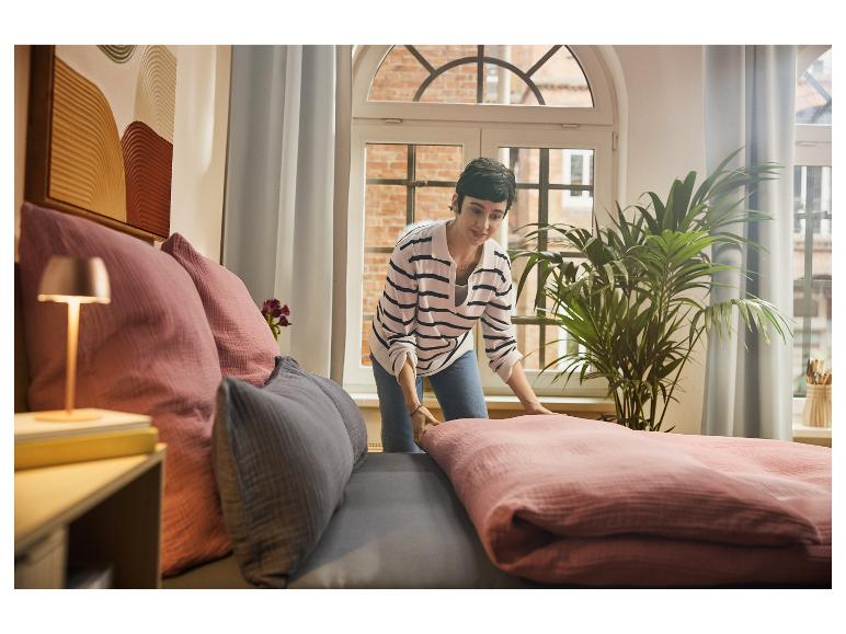 Femme faisant le lit avec une literie rose et des oreillers gris et roses.