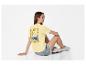 Vrouw in geel T-shirt met 'Ciao Bella'-print en denim shorts, zittend op de grond.