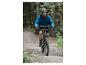 Un homme roule à vélo de montagne sur un chemin de gravier en portant une veste bleue.