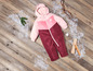 Een roze en rode winterjas voor baby's op een houten vloer met sneeuw.