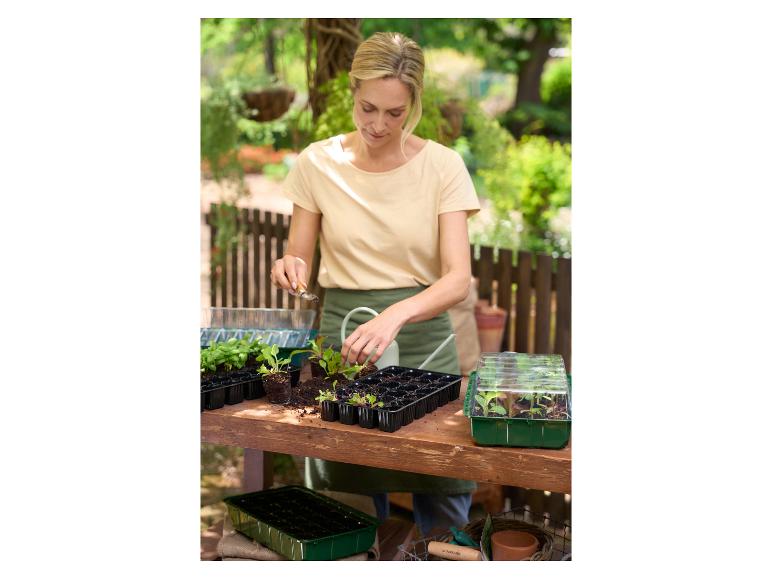Femme plantant des graines dans des plateaux de semis et des mini-serres PARKISDE dans le jardin.