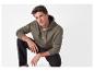 Een jonge man in een olijfgroene hoodie en een zwarte broek.