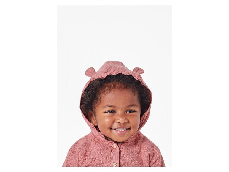 Een baby draagt een roze gebreide trui met capuchon.