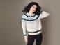 Une femme aux cheveux bouclés porte un pull blanc à motif scandinave et un pantalon noir.