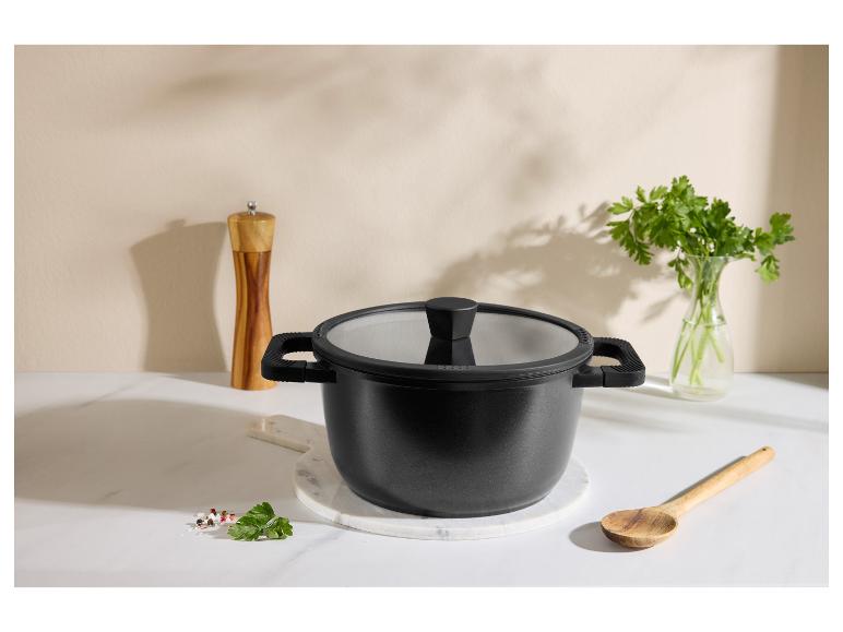 Marmite noire avec couvercle, cuillère en bois, moulin à poivre et persil sur un comptoir de cuisine.