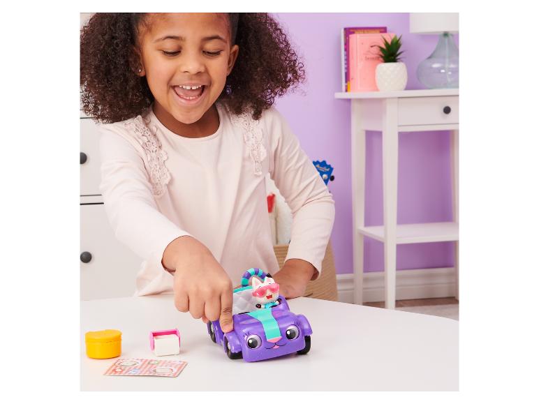 Een meisje speelt met een paars speelgoedvoertuig en een kattenfiguur op een tafel.