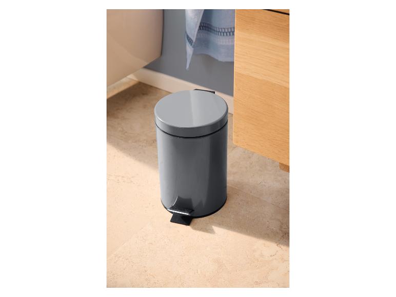 Grijze pedaalemmer in een badkamer met lichte tegels en een houten kast.