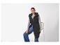 Vrouw in zwarte gewatteerde bodywarmer met capuchon, grijs shirt en jeans, zittend op een stoel.