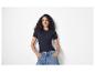 Femme en t-shirt côtelé bleu foncé et jean, mains dans les poches.