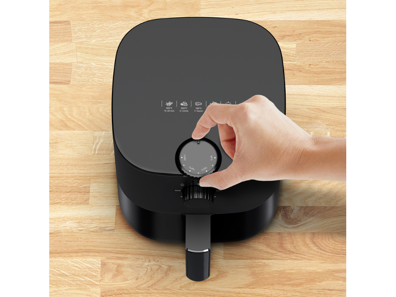 Zwarte airfryer met een hand die de temperatuur aanpast op een houten aanrecht.