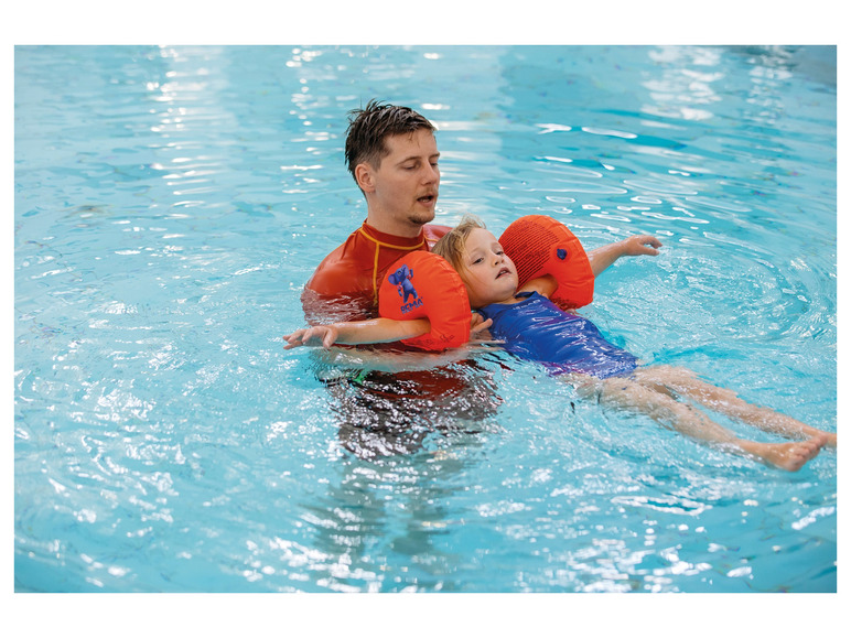 Un enfant apprend à nager dans une piscine avec des brassards de la marque Bema.